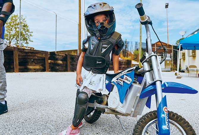 Child with helmet standing next to a dirt bike