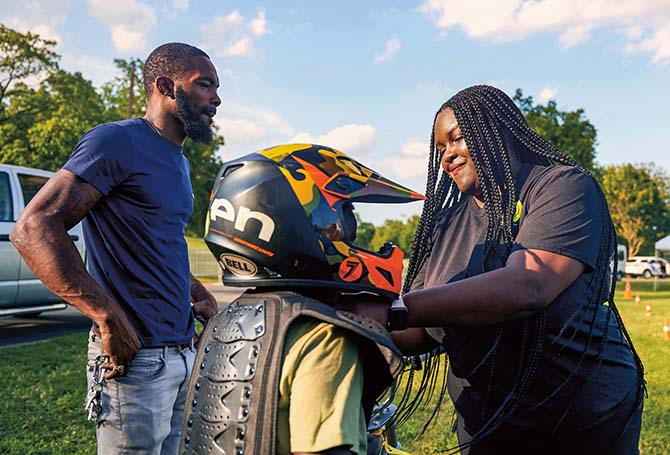 Two people helping a student put on a helmet