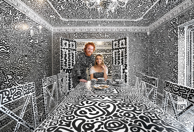 Photo of a couple pictured in their home where all walls & furniture are drawn completely in doodles