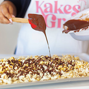 Popcorn in a pan with someone drizzling chocolate on top