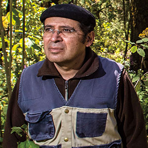 A headshot of a serious looking middle-aged person wearing a beret, glasses, and a jacket