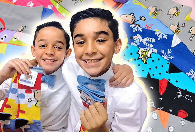 Two kids wearing shirts and bowties with their arms around one another, grinning and holding socks
